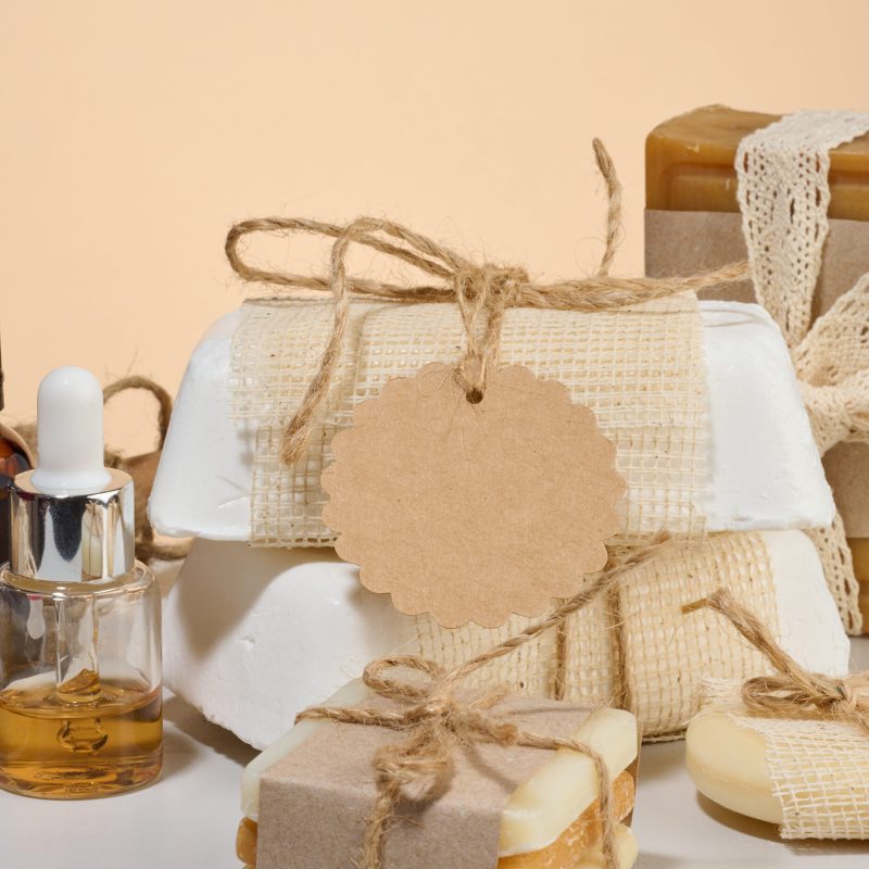 Composition of handmade soap in craft paper, bottles with oil and tags on a neutral background.