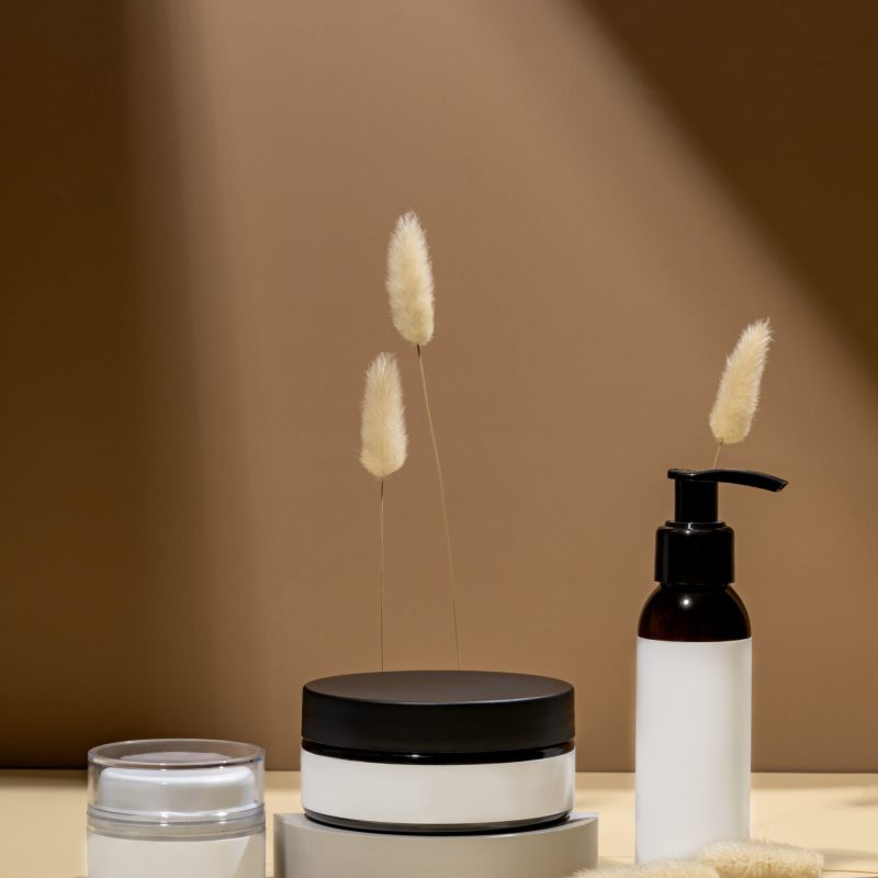 Mock up glass dropper bottles on a white podium on a beige background with hard shadows. Skin care products in trendy presentation.